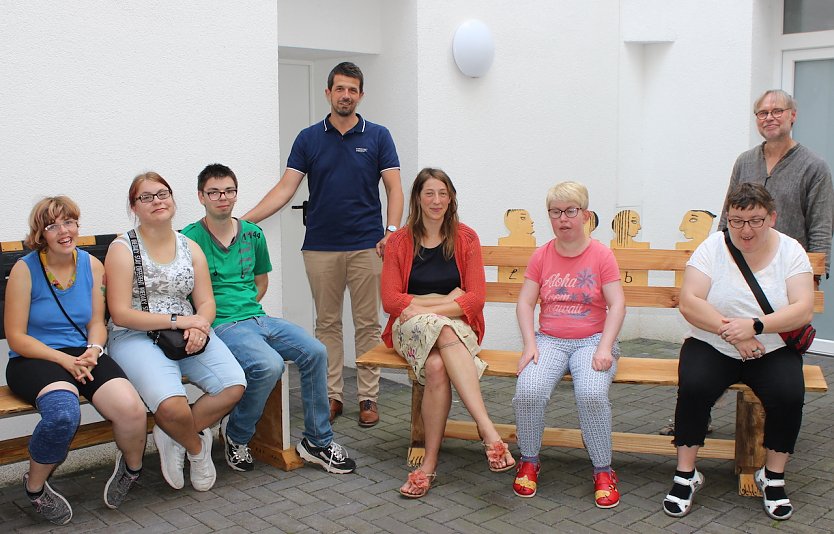 Foto: Lebenshilfe-Mitarbeiter Torsten Rieschel (4.v.l.), Praktikantin Laura Johann (5.v.l.) und Kursleiter Martin Jahn (rechts im Bild) freuen sich, die B&auml;nke an Projektteilnehmern und Hausbewohnern &uuml;bergeben zu d&uuml;rfen. Nicht alle B&auml;nkebauer waren zum Fototermin anwesend. (Foto: NTL)