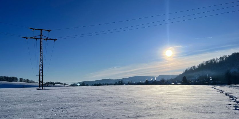 Bild: Ein Hochspannungsmast steht in einer verschneiten Landschaft. 