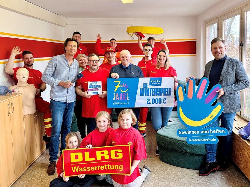 Bild: Mehrere Menschen stehen in einem Raum um halten einen symbolischen Spendenscheck.