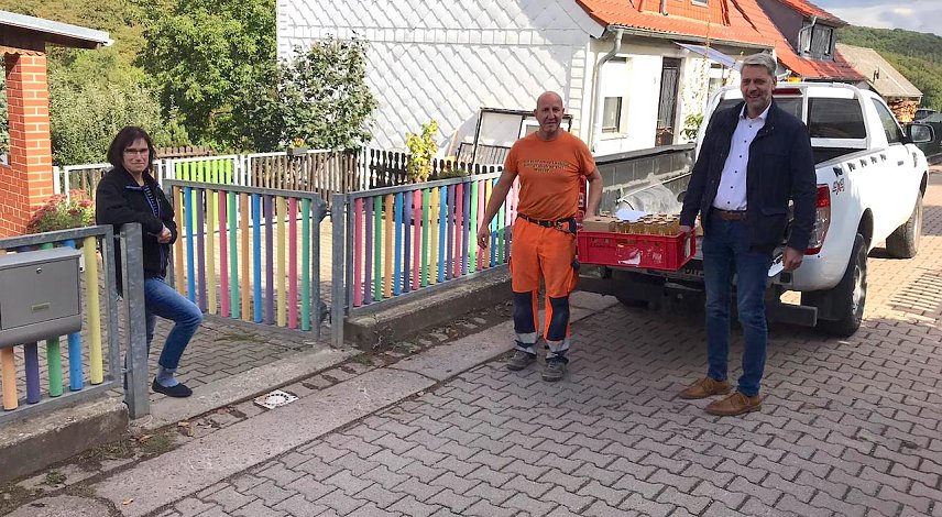 Bild: Silke August, Kitaleiterin in Herrmannsacker, freut sich &uuml;ber die Mostlieferung. Stephan Klante und Mario Schmidt tragen die Kiste in die Kita. 