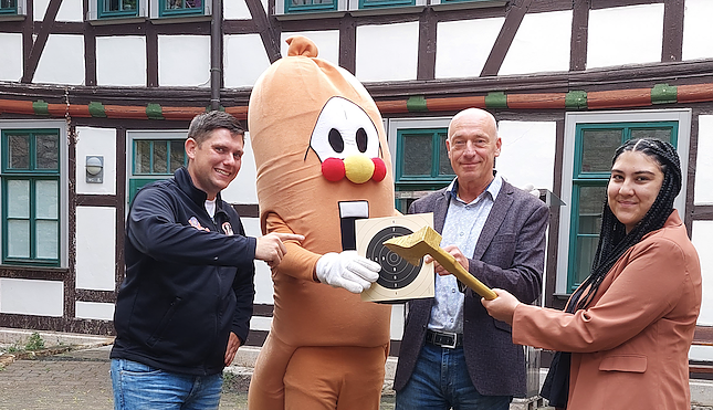 Bild: Markus Edom und Chiara Heller vom Kultur-Referat der Stadt M&uuml;hlhausen, Maskottchen Wurschti und der stellvertretende Gesch&auml;ftsf&uuml;hrer des Bratwurstmuseums, Kay Wipprecht, mit der Goldenen Axt, die bei den Wettbewerben zur Holzfahrt verliehen wird.