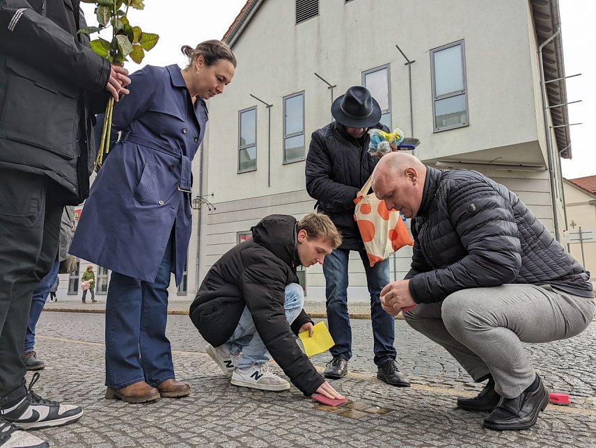 Bild: Sch&uuml;lerinnen und Sch&uuml;ler des Geschwister-Scholl-Gymnasiums k&uuml;mmerten sich in der Hauptstra&szlig;e gemeinsam mit ihrem Lehrer Martin Brauer (2.v.re.), Dr. Carolin Sch&auml;fer, Leiterin des Schlossmuseums (3.v.re hinten), Claudia Langhammer, Leiterin der Stabsstelle Kultur/Wirtschaftsf&ouml;rderung/Tourismus (4.v.re. hinten) und Sondersh&auml;user B&uuml;rgern um das S&auml;ubern der Stolpersteine. 