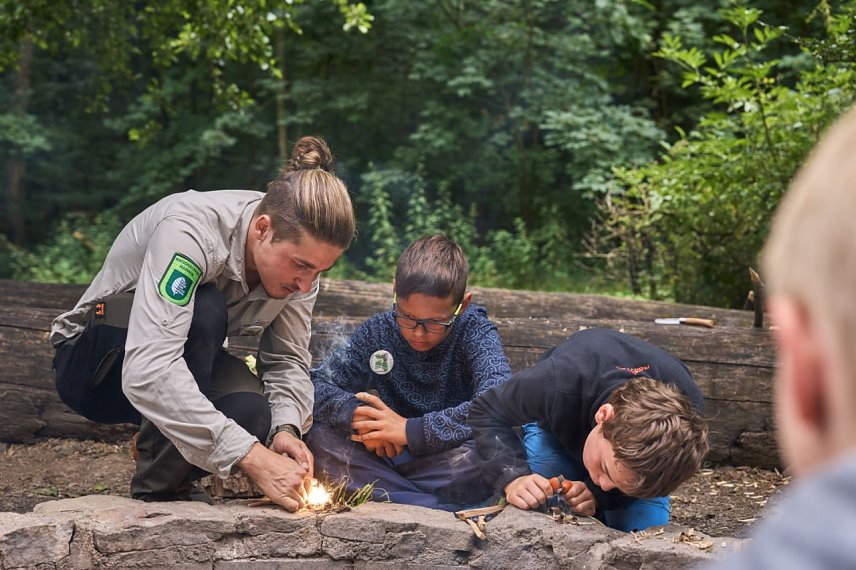 Bild: Vier Tage und drei N&auml;chte sind die Kinder in der Natur des Nationalparks Hainich unterwegs. Im Hintergrund ist eine Schlafstelle zu sehen. Foto: Tino Sieland Hier lernen die Kinder vom Ranger, mit dem Feuerstahl ein Feuer zu entfachen.
