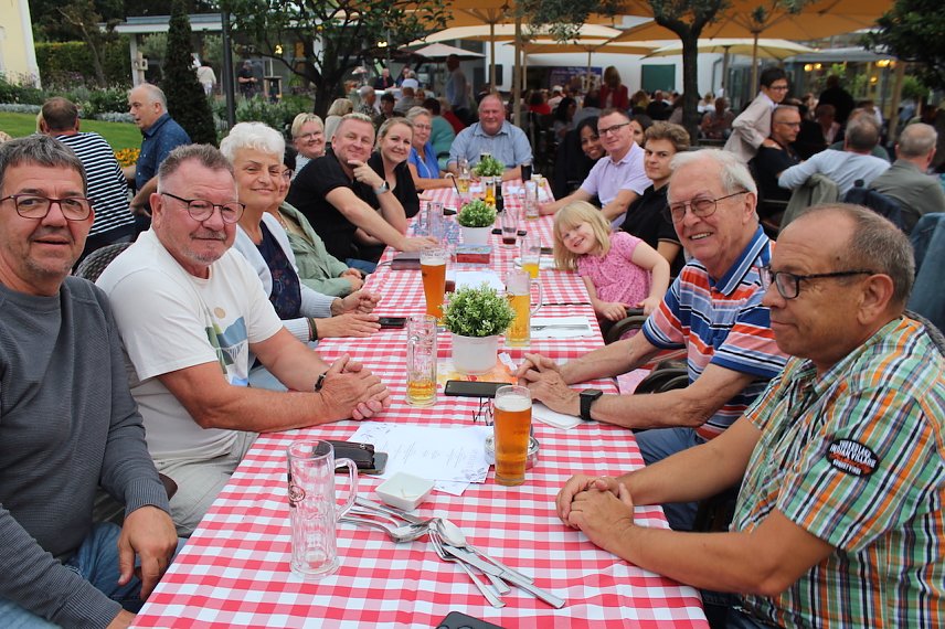 Bild: Fr&ouml;hliche Menschen sitzen bei sch&ouml;nem Wetter an einem Tisch im Freien.
