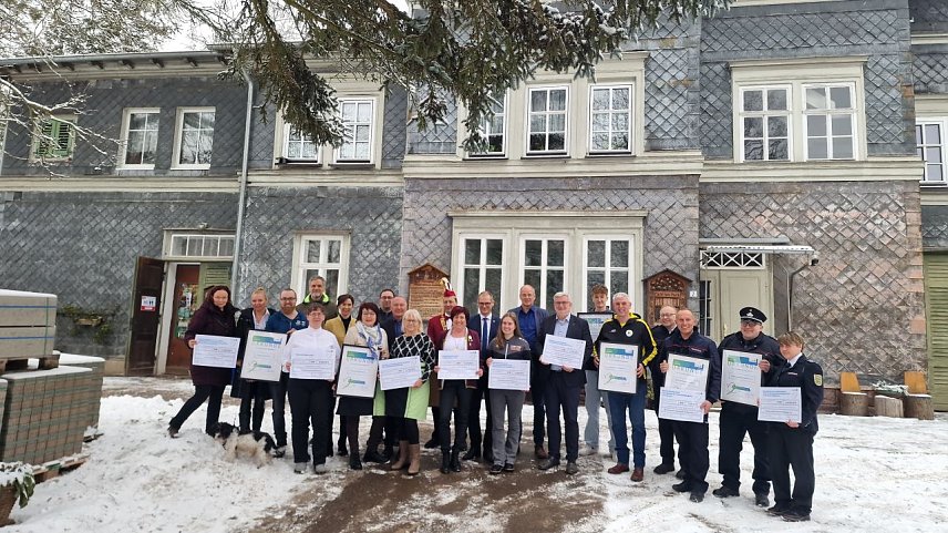 Bild: Ein Gruppenfoto vor dem Kutscherhaus im Park Hohenrode, viele Menschen mit Urkunden und Schecks