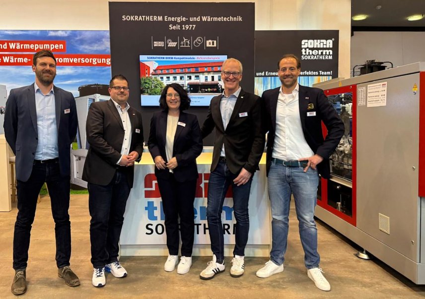 Bild: M&auml;nner und Frauen stehen vor einem gro&szlig;en BHKW-Kompaktmodul.