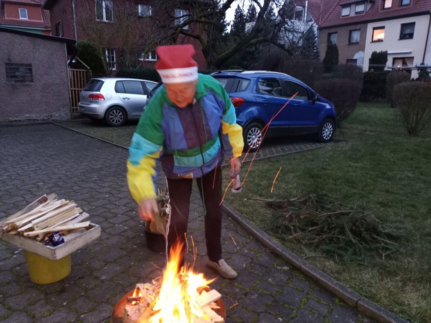 Bild: Volker Wente mit Nikolaus-Zipfelm&uuml;tze f&uuml;ttert die Flammen mit kleinen Fichtenzweigen.