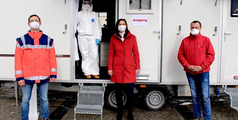 Sandro Bauer (DRK), Sandra Böhme (Rettungsassistentin in Schutzkleidung), Landrätin Antje Hochwind-Schneider und Sven Österheld (DRK) vor dem Testmobil des Kreises (v.l.n.r.) (Foto: emw)