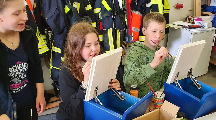 Luisa Rahn, Johanna Bernsdorf und Johann Schütze (v.l.n.r.) von der Jugendfeuerwehr bemalen die Klappen der Stempelkästen. (Foto: Gabriele Knust)