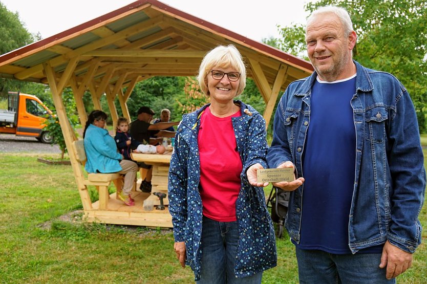 Ortschaftsbürgermeisterin Petra Gerlach und Zimmermann Mario Eckert vor der neuen Waldschenke. Das Schild wurde an der Sitzgruppe angebracht und erinnert daran, dass der Ilfelder Ortschaftsrat diese gesponsert hat.  (Foto: Gemeinde Harztor/Susanne Schedwill)