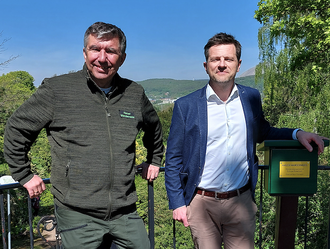 Klaus Dumeier (links im Bild), Geschäftsführer der Harzer Wandernadel übergab den nagelneuen tannengrünen Stempelkasten an seinem Standort, dem Alpinum im Europa-Rosarium Sangerhausen, an Matthias Grünberg, den Geschäftsführer der Rosenstadt Sangerhausen.  (Foto: Europa-Rosarium)