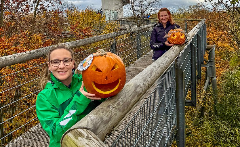 Sandy-Ann Bergmann und Diana Ludwig (v.l.n.r.) vom Team des Baumkronen- pfades präsentieren zwei schaurig schöne Kürbisgesichter.  (Foto: KTL Kur und Tourismus Bad Langensalza GmbH)